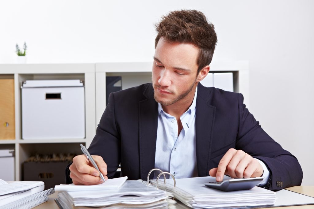 Man sitting at a table with a calculator, pen, and paper 